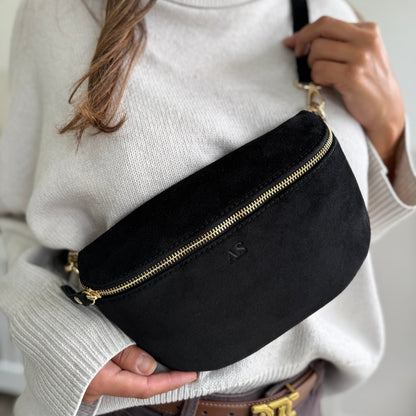 Person wearing a black waist bag with a gold zipper against a neutral background