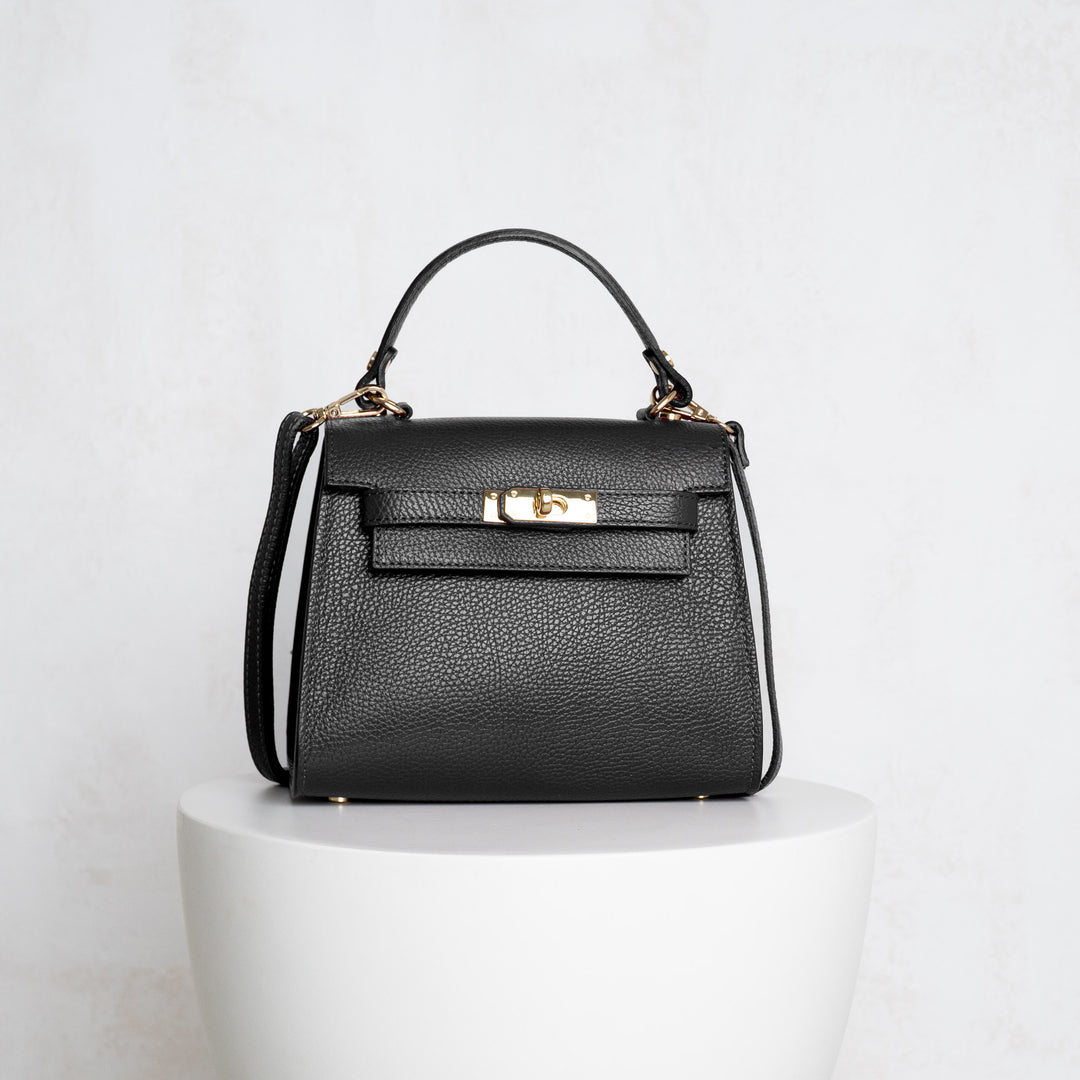 Black handbag with gold accents on a white pedestal against a light gray background