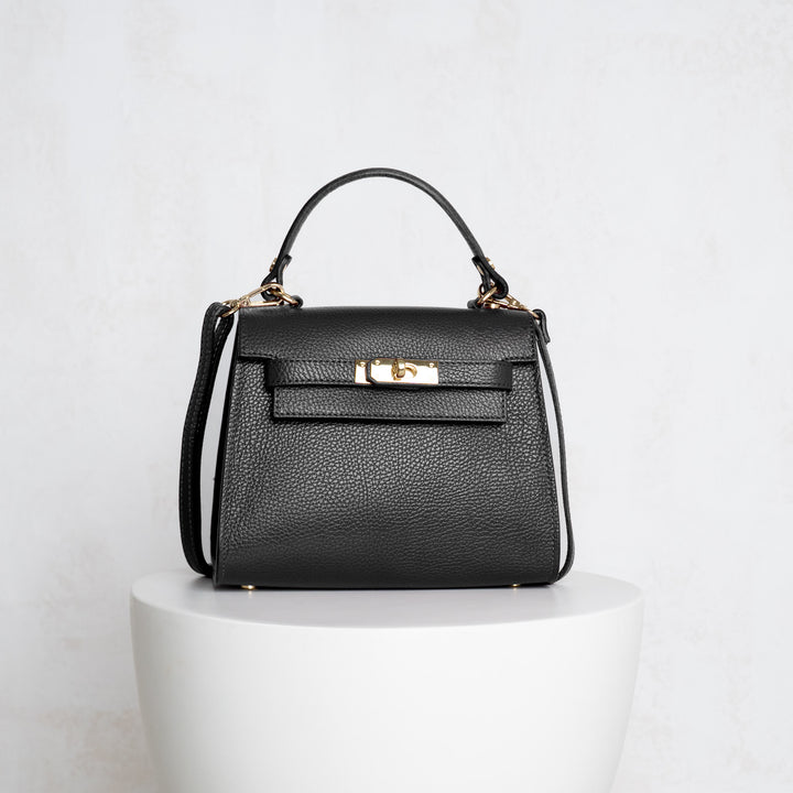 Black handbag with gold accents on a white pedestal against a light gray background