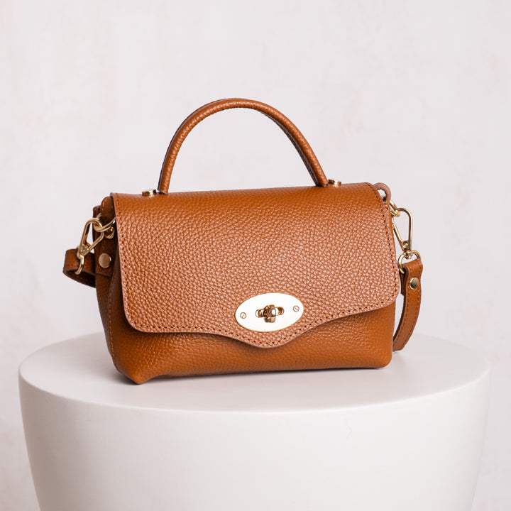 Brown leather handbag with gold accents on a white pedestal