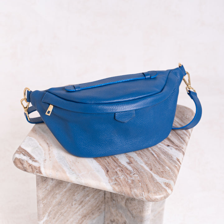 blue leather bumbag with gold hardware on marble table 