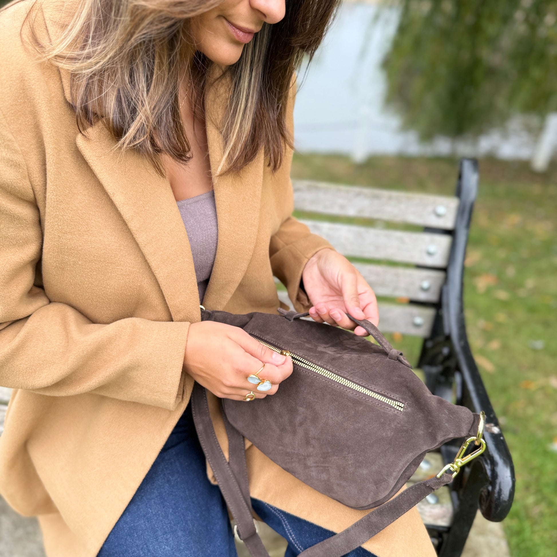 Woman in a beige coat sitting on a bench with a brown bumbag